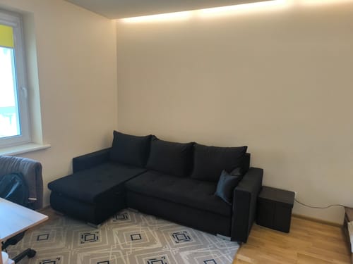Kliento tamsus minkštas kampas LOKO, pastatytas kambaryje ant raštuoto kilimo.