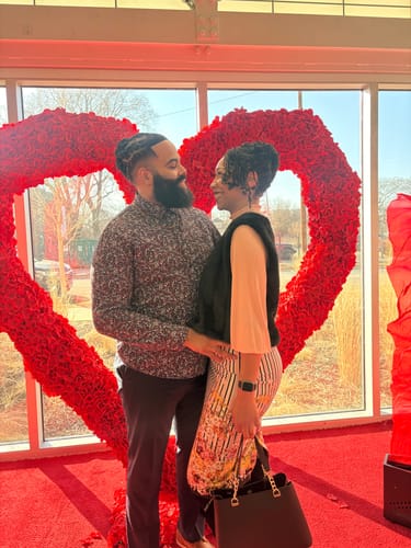 Customer and partner pose happily before a red heart, celebrating their Valentine's weekend with a custom song.