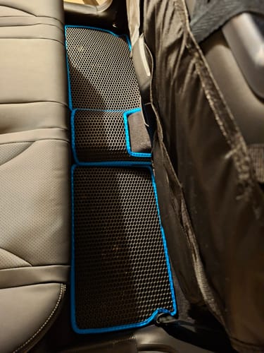 Recenzent pokazuje czarny, dopasowany dywanik samochodowy z niebieskim obszyciem, położony na podłodze z tyłu samochodu.