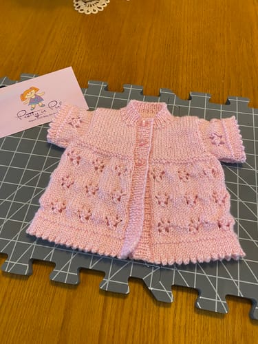 Customer's hand-knitted pink baby cardigan from the kit, laid flat to display its delicate lacy pattern.