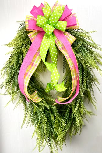 Customer's Draped Button Fern Wreath shown decorated with a large pink and green bow.
