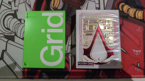 Customer displays the two decks from their Mystery Deck purchase: a green Grid deck and a decorative Assassin's Creed deck.