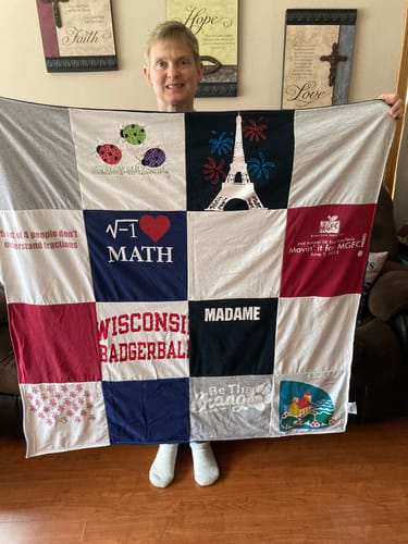 Customer holding up their finished Premium T Shirt Quilt, showing various colorful t-shirt designs.