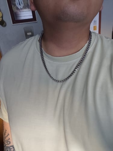 Un cliente muestra su cadena Cuban Link de 8 mm sobre una camiseta de color claro.