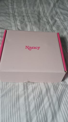 Customer's closed pink box for the Lem Clitoral Massager sitting on a striped bedspread.
