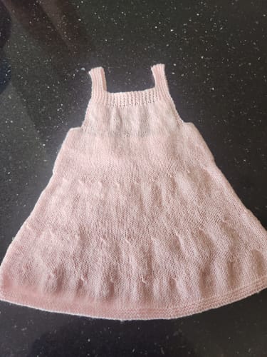 Reviewer's finished Sirdar 6172 Baby Pinafore, knitted in a light pink yarn and laid flat.