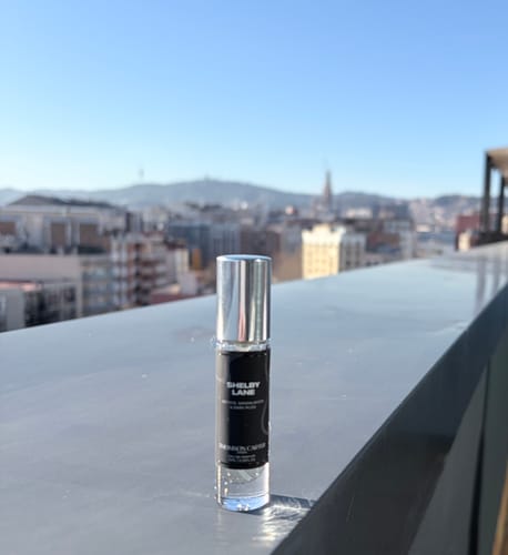 Customer's Shelby Lane Eau de Parfum rollerball on a ledge overlooking a sunny Barcelona city skyline.