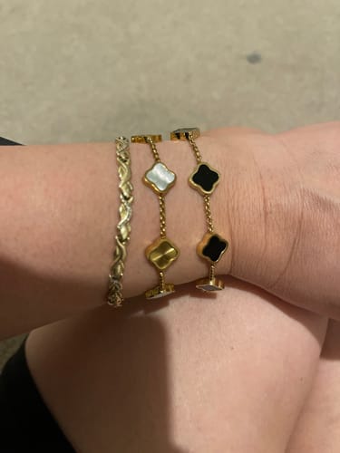 Customer's wrist showing two Celine Clover Bracelets, one with white mother of pearl and one with black enamel motifs.