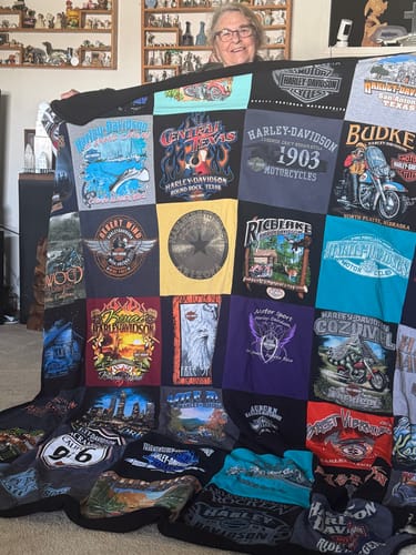 A reviewer proudly holds up her large Premium T Shirt Quilt, made from many Harley-Davidson themed shirts from her travels.