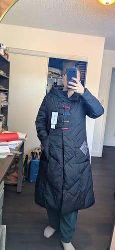 Reviewer's front view of the black padded long coat, showing the colorful toggles and new tags still attached.