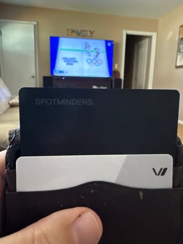 Customer holding a wallet with the black SPOTMINDERS tracking card visible inside.