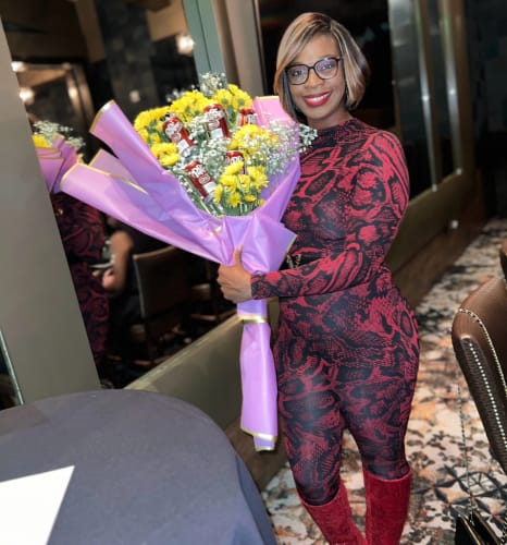 Customer wearing the red snakeskin Naked Print Closed Toe Jumpsuit while holding a large bouquet of flowers.