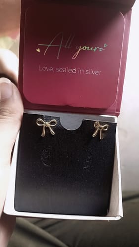 Reviewer holding the open jewelry box showing the golden Tied with Love bow-knot earrings.
