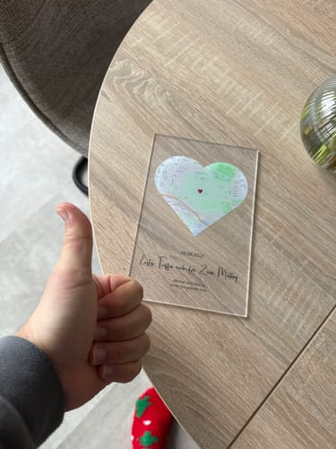 Ein Rezensent gibt einen Daumen hoch neben der personalisierten Acryltafel, die auf einem Holztisch liegt.