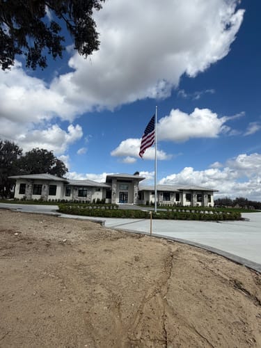 Reviewer's installed Commercial Flagpole with a waving American flag, seen from a distance in front of a home.