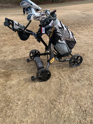 Customer's Club Booster V2Pro attached to a push cart with a full golf bag on dormant grass.