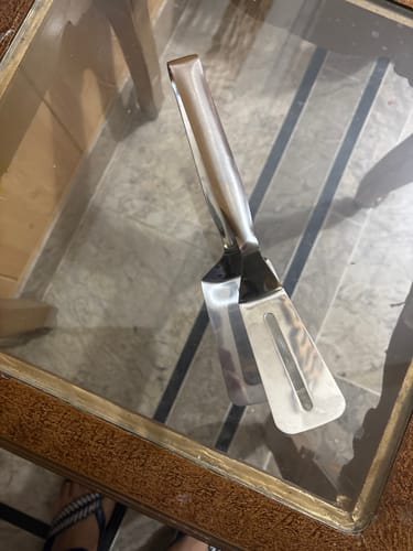 Customer's new Spatula Tong made of shiny metal, resting on a glass-topped table.