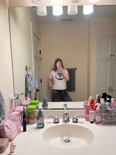 Reviewer taking a mirror selfie, wearing the graphic studio 54 baby tee with dark pants in a bathroom.