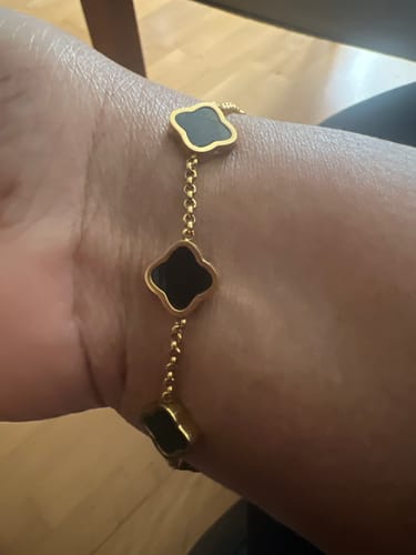 Customer showing a gold-tone bracelet with black clover-shaped charms on their wrist.