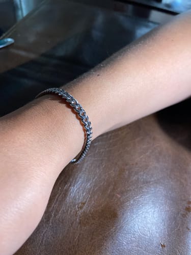 Cliente luciendo la Pulsera Miami Cuban de 5mm en su muñeca sobre una superficie de cuero marrón.
