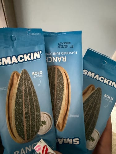 Customer's hand holding three bags of Smackin' Ranch flavored sunflower seeds.