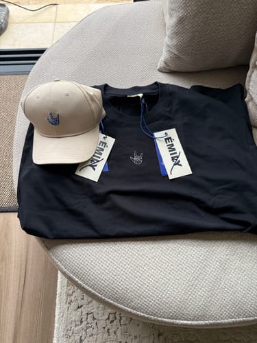 תמונת ביקורת המציגה טי שירט LOUDER by Émily שחורה וחדשה, מונחת על רהיט עם תוויות.