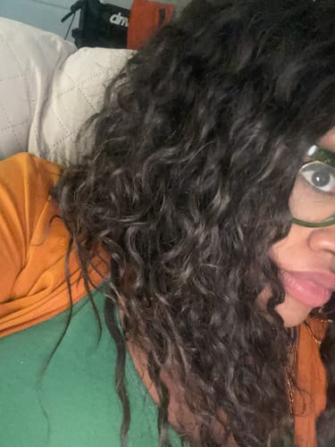 Close-up of a reviewer showing the long, dark natural curls of her Bohyme Birth Remi hair weave.