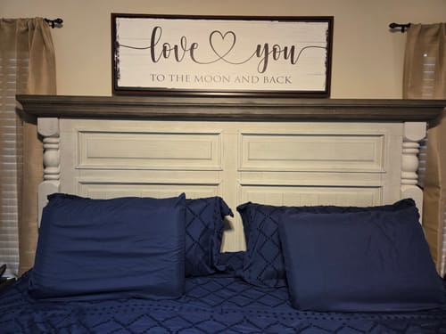 Customer's Love You To The Moon And Back Sign hanging on the wall above a large bed headboard.