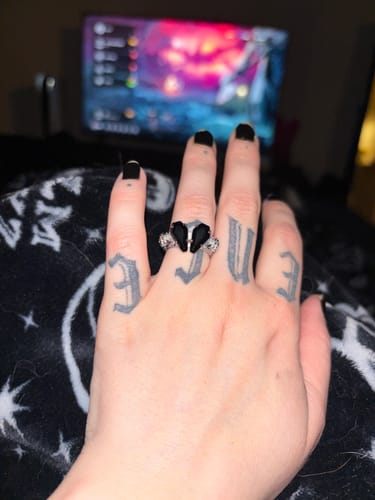 Reviewer's tattooed hand with black nails wearing the PROMISE RING, which has two black coffin-shaped stones.