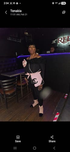 Reviewer posing in the black Naked Off-Shoulder Roses Jumpsuit in a dimly lit room.