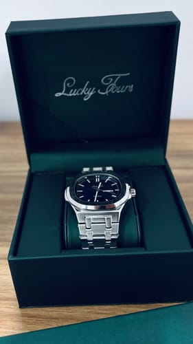 Customer's silver Lucky Fours® Brone watch with a black dial, shown inside its open green presentation box.
