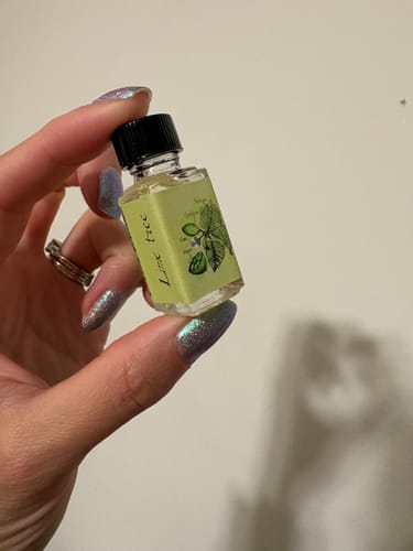 Reviewer holds a small glass bottle of perfume oil with a light-green label.