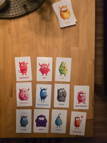 Rezensent legt die Edubini Gefühlskarten auf einen Holztisch. Jede Karte zeigt ein buntes Monster, das eine andere Emotion darstellt.