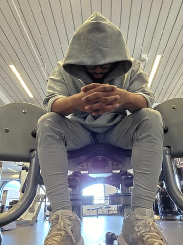 Reviewer wearing the grey Megàlo 3/5 Sleeve Hoodie with the hood up, sitting on gym equipment.
