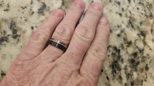 Customer's hand resting on a counter, wearing The Brutalist ring with its black band and rose gold inlay.