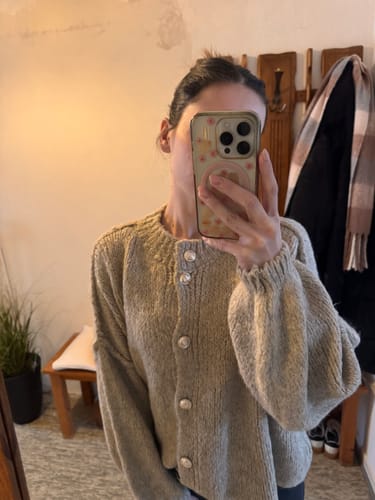 Kundin macht ein Spiegelselfie und trägt den beigen „CozyGlam“ Cardigan mit Ballonärmeln.