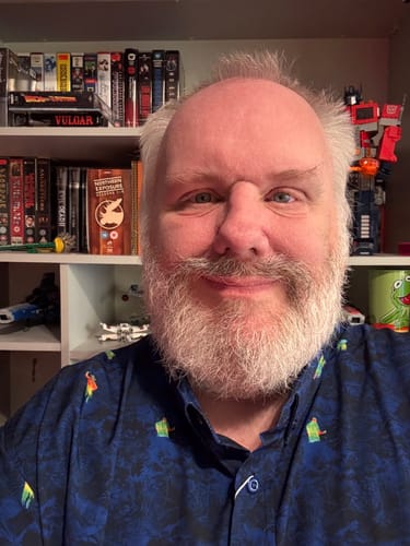 Reviewer smiling while wearing the dark blue Predator "Thermal Vision" KUNUFLEX button-down shirt in front of bookshelves.