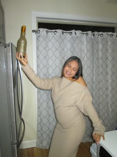 Reviewer happily posing in the beige Knit Off-Shoulder Sweater Maxi Dress indoors.