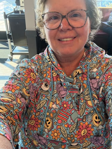 Reviewer smiling in a selfie wearing the colorful, patterned Happy Dazed hoodie.