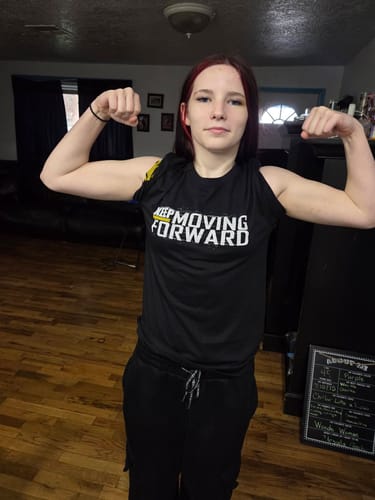 Customer flexing their arms while wearing the black Keep Moving Forward t-shirt in a living room.