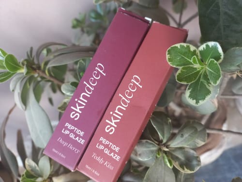 Customer's packaging for the Peptide Lip Glaze in shades Deep Berry and Teddy Kiss, resting among green leaves.