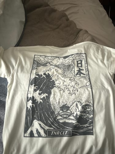 Customer's white VOLCANIC WAVES TEE laid flat, showing the large Japanese-style wave graphic on the back.