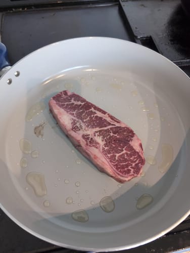 Customer's raw, well-marbled Halal New York Steak in a pan with oil before cooking.
