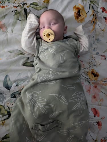 A customer's baby sleeping peacefully in the green 4 Season Ultimate Baby Sleep Bag with a leaf print.
