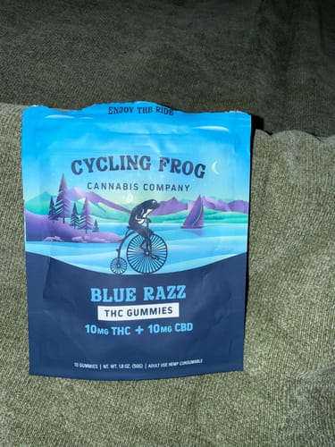 Reviewer's blue pouch of Cycling Frog's Blue Razz THC Gummies resting on a green textured surface.