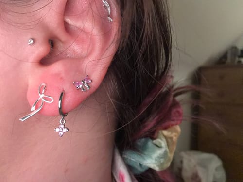 Customer's ear with the dangling Lucky Charm Pink/Silver huggie, stacked next to a silver bow earring.
