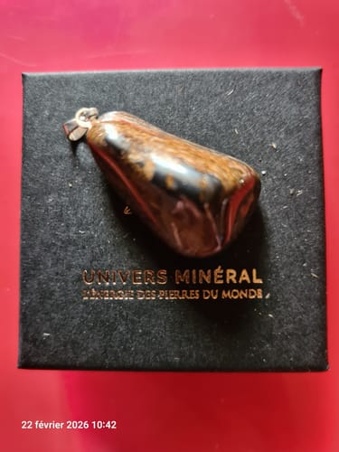Client présentant son pendentif Bronzite poli, posé sur sa boîte de présentation noire.