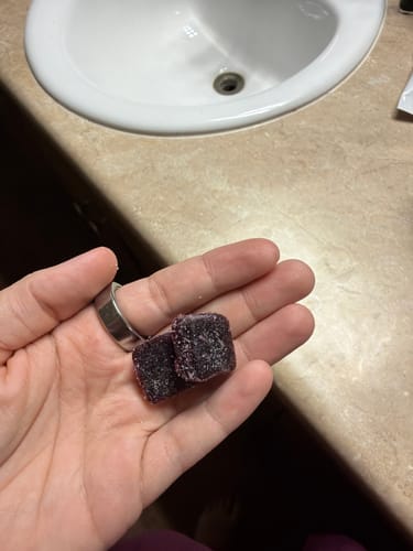 Reviewer's hand holding two dark, sugared Black Currant Nighttime Gummies.