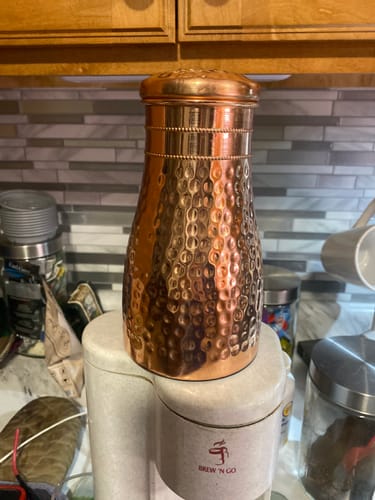 Customer's shiny hammered Himalayan Ayurvedic Bedside Carafe with its lid on, placed on a kitchen counter.