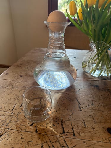 Rezensent zeigt sein wunderschönes ND MYTHOS Glas auf einem Holztisch neben einer Glaskaraffe.